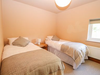 A bedroom with two single beds a wooden nightstand and a window at The Firs in Wendling near Dereham