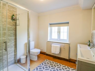 A bathroom with a shower enclosure, toilet, sink, radiator with a towel, and a window at The Firs in Wendling near Dereham