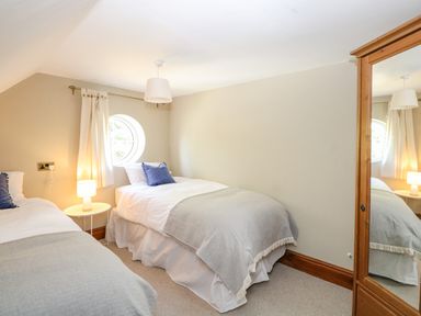 A bedroom with two single beds a round window and a wooden wardrobe at The Firs in Wendling near Dereham