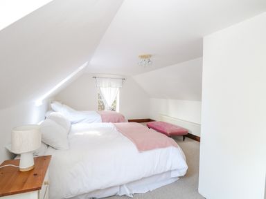 A bedroom with two beds a bedside table with a lamp a window and a pink bench at The Firs in Wendling near Dereham