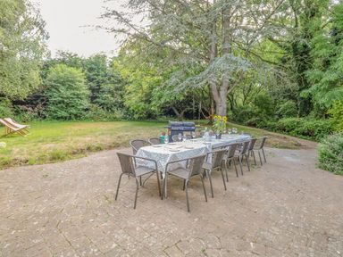 An outdoor patio with a long dining table set for a meal surrounded by chairs and trees at The Firs in Wendling near Dereham