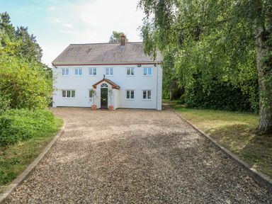 A white two-story house with a gravel driveway surrounded by greenery at The Firs in Wendling near Dereham