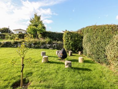 An outdoor garden area with logs arranged in a circle around a covered fire pit at Tegfryn Bach in Llangoed near Beaumaris