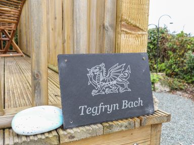 A black slate sign with a dragon illustration and Tegfryn Bach text on a wooden deck at Tegfryn Bach in Llangoed near Beaumaris