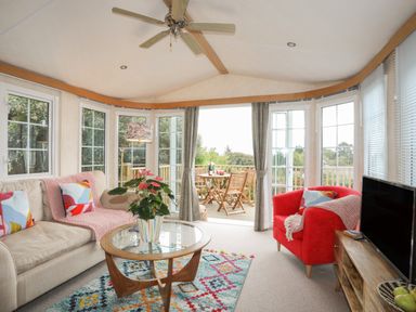 A living room with a beige sofa, red armchair, glass coffee table, colorful rug, ceiling fan, and TV at Tegfryn Bach in Llangoed near Beaumaris