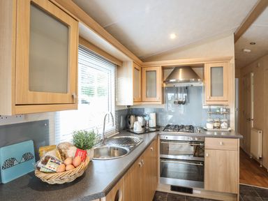 A kitchen with wooden cabinets a stainless steel oven and stove a window with blinds and a basket with eggs and bread on the counter at Tegfryn Bach Llangoed near Beaumaris