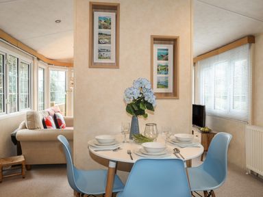 A dining area with a round table set for four with blue chairs and a living room with beige sofas in a room at Tegfryn Bach in Llangoed near Beaumaris