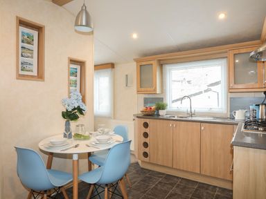 A kitchen with a round dining table set with dishes blue chairs and wooden cabinets at Tegfryn Bach in Llangoed near Beaumaris