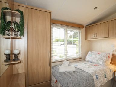A small bedroom with a single bed a window with blinds and wooden cabinets at Tegfryn Bach in Llangoed near Beaumaris