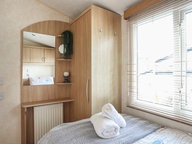 A bedroom corner with a wooden wardrobe mirror shelves and window blinds at Tegfryn Bach in Llangoed near Beaumaris