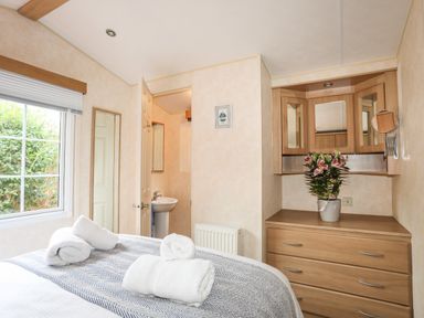 A bedroom with a bed with rolled towels a window a mirror a dresser with flowers and an open door leading to a bathroom at Tegfryn Bach in Llangoed near Beaumaris