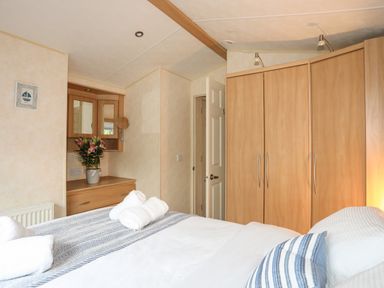 A bedroom with a bed with white and striped bedding a wooden wardrobe and a wooden dressing table with flowers at Tegfryn Bach in Llangoed near Beaumaris