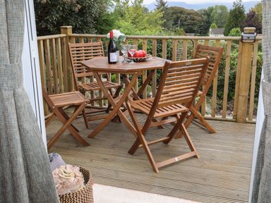 A wooden outdoor table with four chairs on a deck with a bottle of wine glasses and fruit at Tegfryn Bach in Llangoed near Beaumaris
