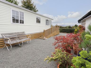 A gravel path with a wooden bench and potted plants beside a mobile home at Tegfryn Bach in Llangoed near Beaumaris