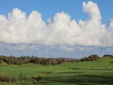 A golf course with a red flag on the green under a blue sky with large white clouds at Tegfryn Bach in Llangoed near Beaumaris