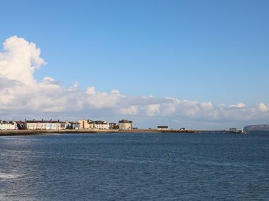 A coastal town with colorful buildings along the shoreline and a pier extending into the sea at Tegfryn Bach in Llangoed near Beaumaris