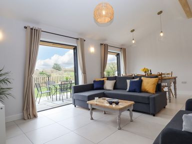 A living room with a gray sectional sofa a wooden coffee table and a dining table with chairs at Woodpecker Lodge in Butterleigh