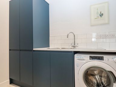 A laundry room with blue cabinets a stainless steel sink a white washing machine and a framed picture on the wall at Woodpecker Lodge in Butterleigh