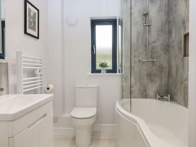 A bathroom with a toilet sink towel rack and bathtub with shower at Woodpecker Lodge in Butterleigh