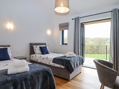 A bedroom with two single beds blue pillows white towels and an open door to a balcony at Woodpecker Lodge in Butterleigh
