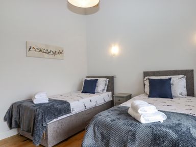 A bedroom with two single beds bedside table and stacked towels at Woodpecker Lodge in Butterleigh