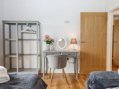 A bedroom with a gray open wardrobe, a gray desk with a mirror and lamp, and part of two beds at Woodpecker Lodge Butterleigh