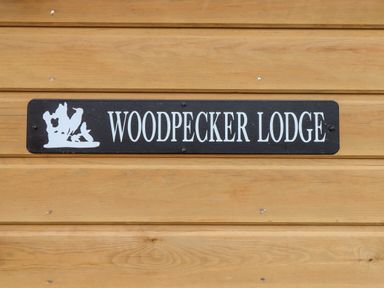 A wooden wall with a black sign reading woodpecker lodge with a woodpecker image