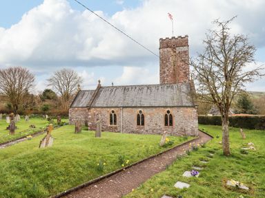 An old stone church with a tower and stained glass windows surrounded by a grassy graveyard with tombstones and a paved walkway