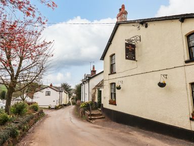 A narrow village street with white houses and a pub sign on a building at The Butterleigh Inn in Butterleigh