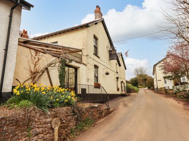 A street with cottages and yellow flowers planted along a stone wall at Woodpecker Lodge in Butterleigh