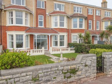 A row of brick houses with bay windows and front gardens behind a stone wall at Weymouth Bay Apartment A Weymouth
