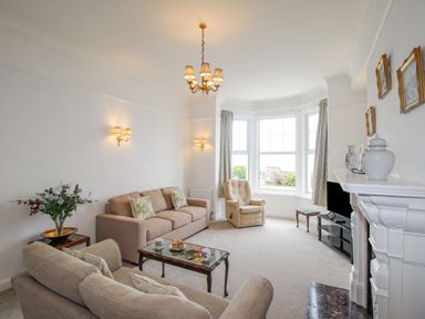 A living room with sofas a glass coffee table an armchair a fireplace and a bay window at Weymouth Bay Apartment A Weymouth