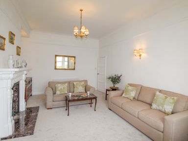 A living room with two beige sofas a fireplace a coffee table with cups and snacks and a wall mirror at Weymouth Bay Apartment A in Weymouth