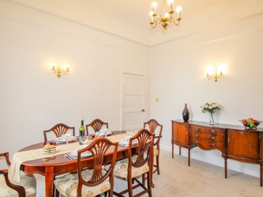 A dining room with a wooden table set for six people and a wooden sideboard with decorations at Weymouth Bay Apartment A in Weymouth