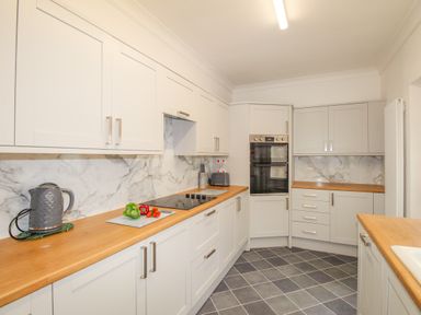A kitchen with white cabinets wooden countertops a kettle toaster double oven and vegetables on the counter at Weymouth Bay Apartment A in Weymouth