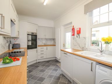 A kitchen with white cabinets black tiled floor wooden countertops a washing machine and vegetables on the counter at Weymouth Bay Apartment A in Weymouth
