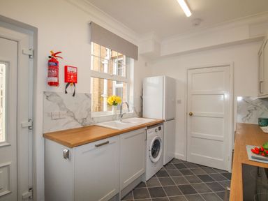A kitchen with a sink washing machine refrigerator fire extinguisher and fire blanket at Weymouth Bay Apartment A in Weymouth