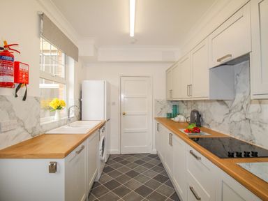 A kitchen with white cabinets wooden countertops a washing machine a stove and a refrigerator at Weymouth Bay Apartment A in Weymouth
