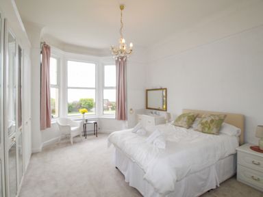A bedroom with a bed side tables armchair small table chandelier and large windows at Weymouth Bay Apartment A in Weymouth