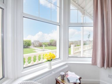 A corner window with white frames overlooking a garden with a stone balustrade and green lawn at Weymouth Bay Apartment A Weymouth