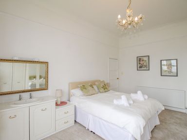 A bedroom with a double bed two folded towels white furniture a large mirror and two paintings on the wall at Weymouth Bay Apartment A in Weymouth
