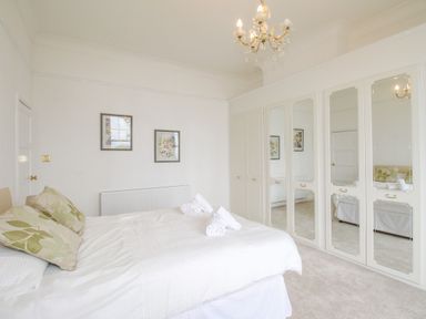 A bedroom with a double bed with cushions and rolled towels next to a wall with floral pictures and mirrored wardrobes at Weymouth Bay Apartment A in Weymouth