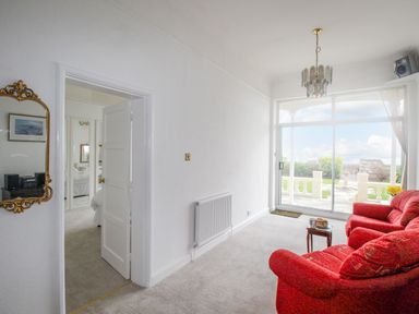 A sitting room with red armchairs a small table and a large window overlooking a garden at Weymouth Bay Apartment A Weymouth