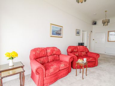A sitting room with two red sofas, a small wooden table with teacup and pastries, and side tables with flowers at Weymouth Bay Apartment A Weymouth