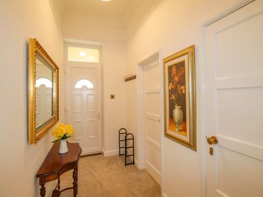 A hallway with a wooden table holding a vase of yellow flowers a large framed mirror a floral painting a door with a coat rack and a shoe rack at Weymouth Bay Apartment A in Weymouth