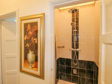 A tiled shower with a showerhead and a framed flower painting on the wall outside in Weymouth Bay Apartment A Weymouth