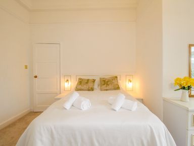 A bedroom with a double bed with rolled towels and floral cushions at Weymouth Bay Apartment A in Weymouth