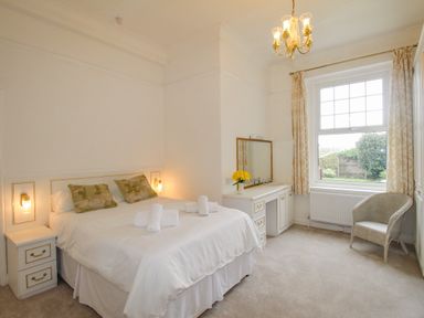 A bedroom with a double bed with pillows and towels bedside tables a dressing table with a mirror a chair and a window at Weymouth Bay Apartment A in Weymouth