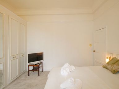 A bedroom with a bed with folded towels and a pillow a small wooden table with a television and built-in wardrobes at Weymouth Bay Apartment A in Weymouth