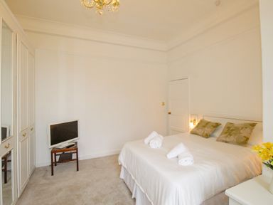 A bedroom with a bed and rolled towels on it a television on a small table a chandelier and built in wardrobes at Weymouth Bay Apartment A Weymouth